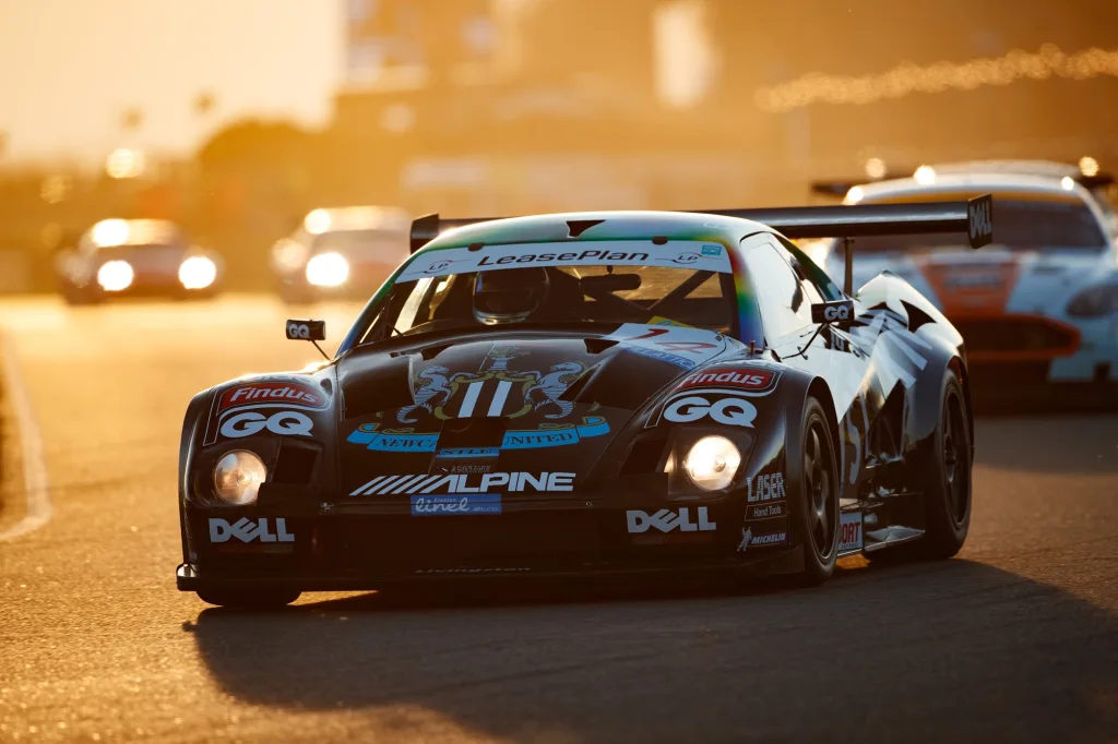 a lister storm race car driving at goodwood in the sunset at the 80th members meeting